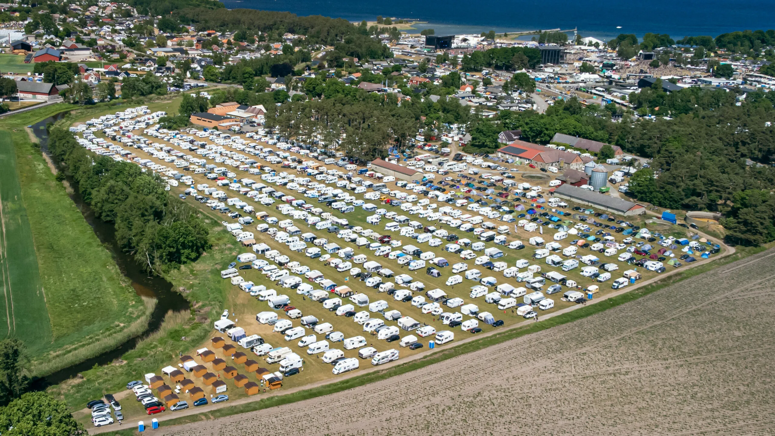 Flygbild över Ingemans Camping med stugbyn längst ner till vänster och festivalområdet vid vattnet i bakgrunden